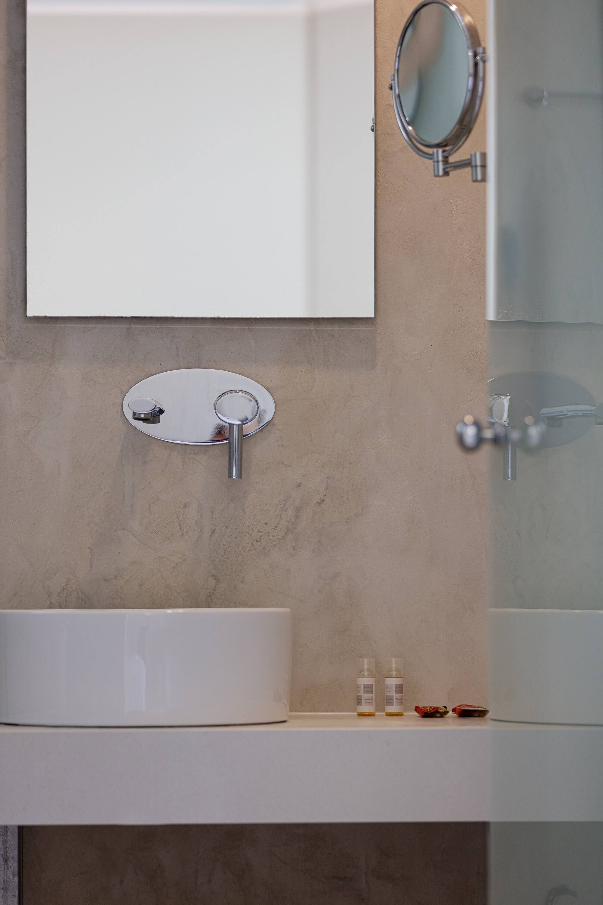 A bathroom with a white sink, a round mirror, and a glass shower enclosure.