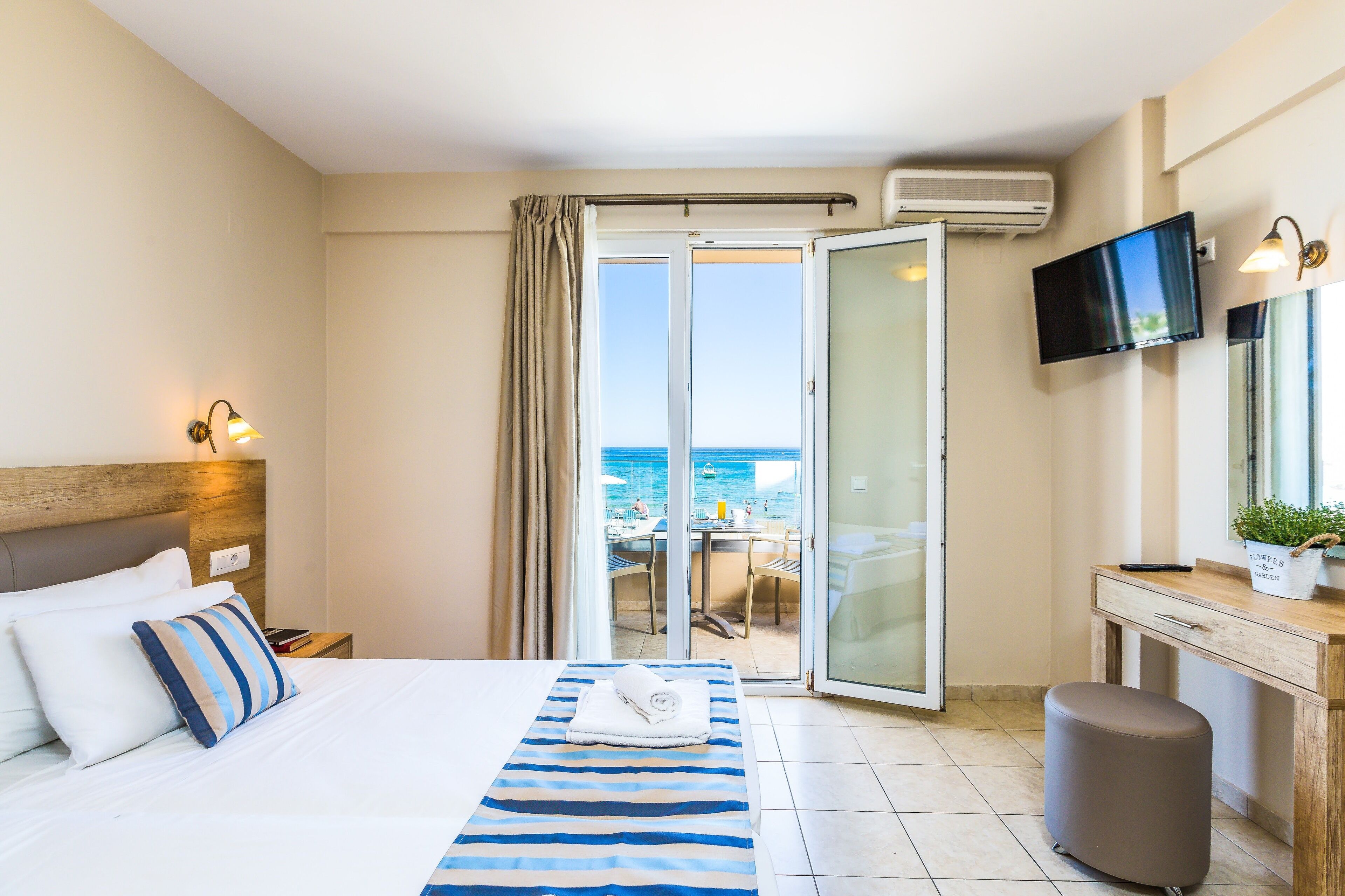 Habitación de hotel con cama, escritorio, televisor y balcón con vista al mar.