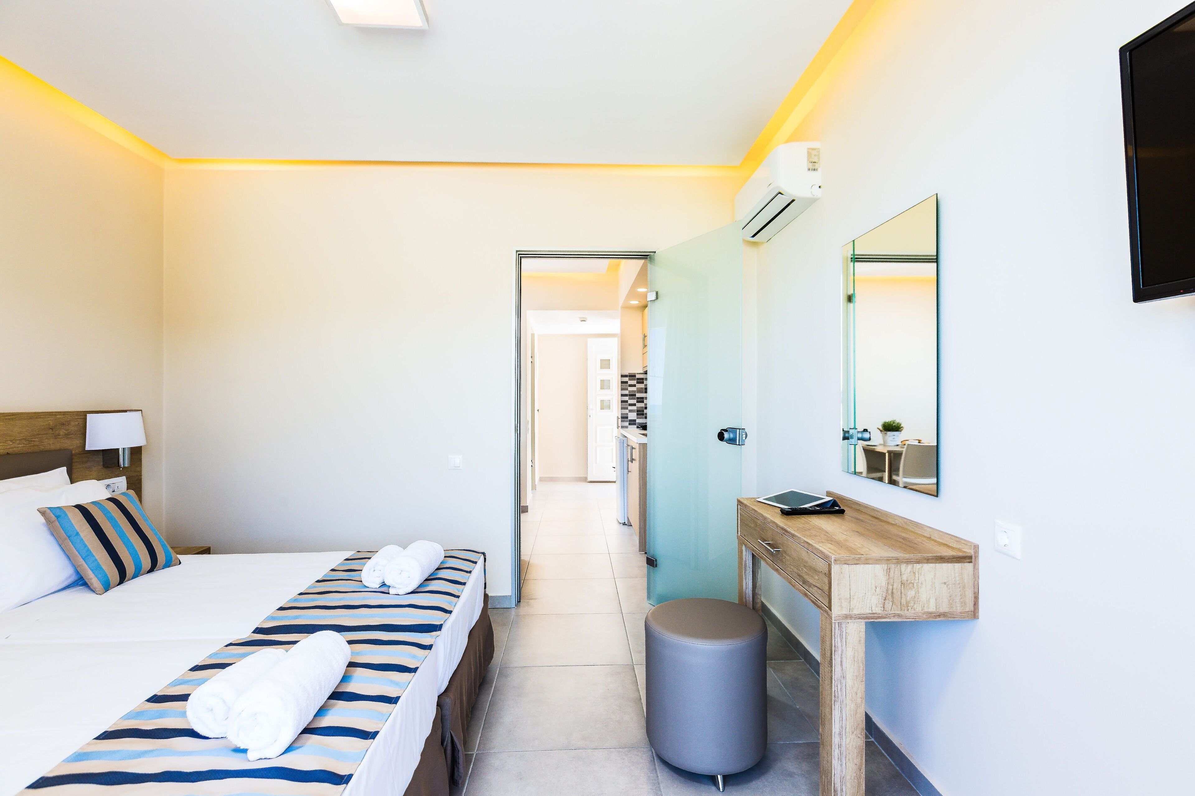 A hotel room with a bed, a bedside table, a mirror, and a small stool.