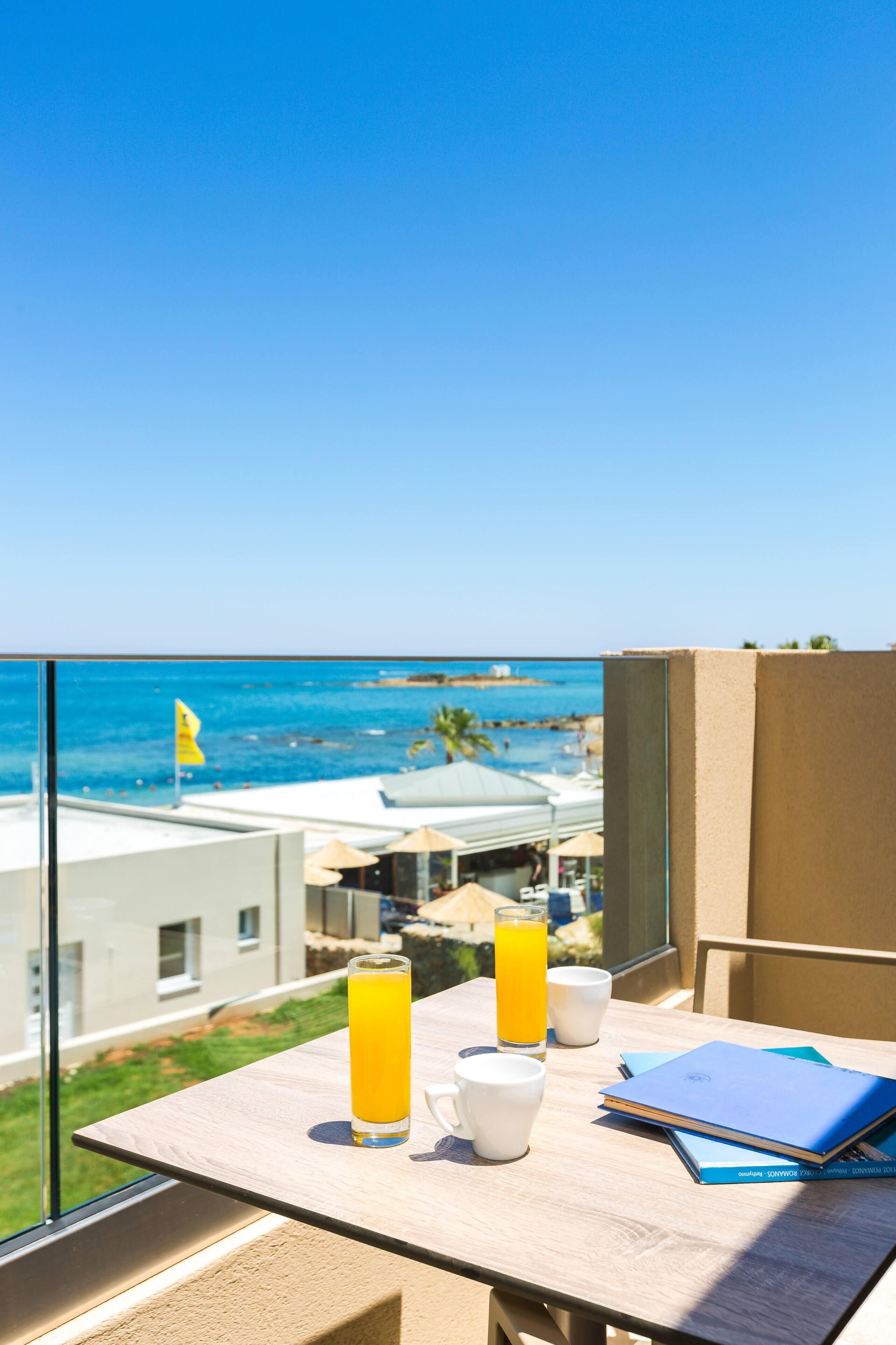 Un balcón con una mesa lista para el desayuno, con vista a una playa y al océano.