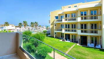 Un hotel de varios pisos con balcones, un césped bien cuidado y una vista despejada al mar.
