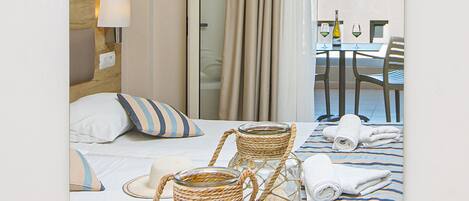 Habitación de hotel con una cama, una lámpara de noche, una cesta de mimbre y vistas al balcón con una mesa y sillas.