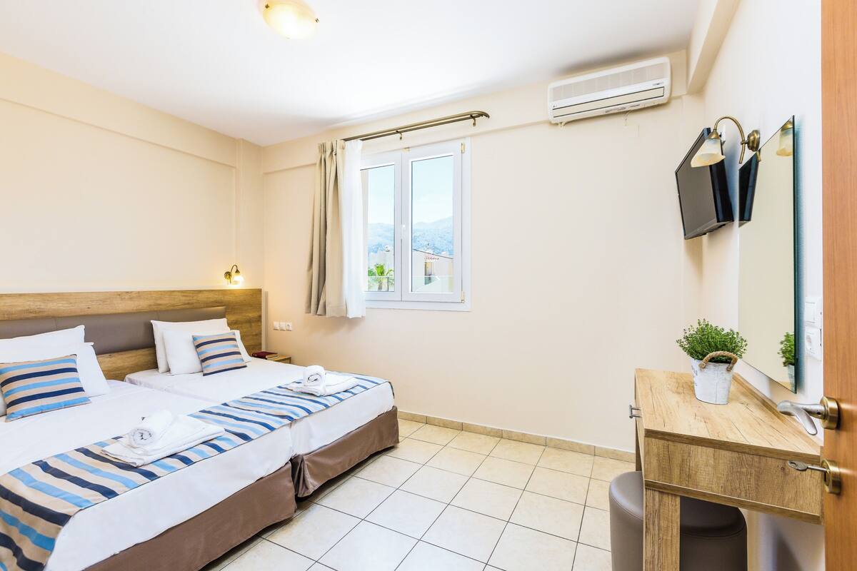 Een hotelkamer met een bed, een bureau, een spiegel en een raam met uitzicht op de bergen.