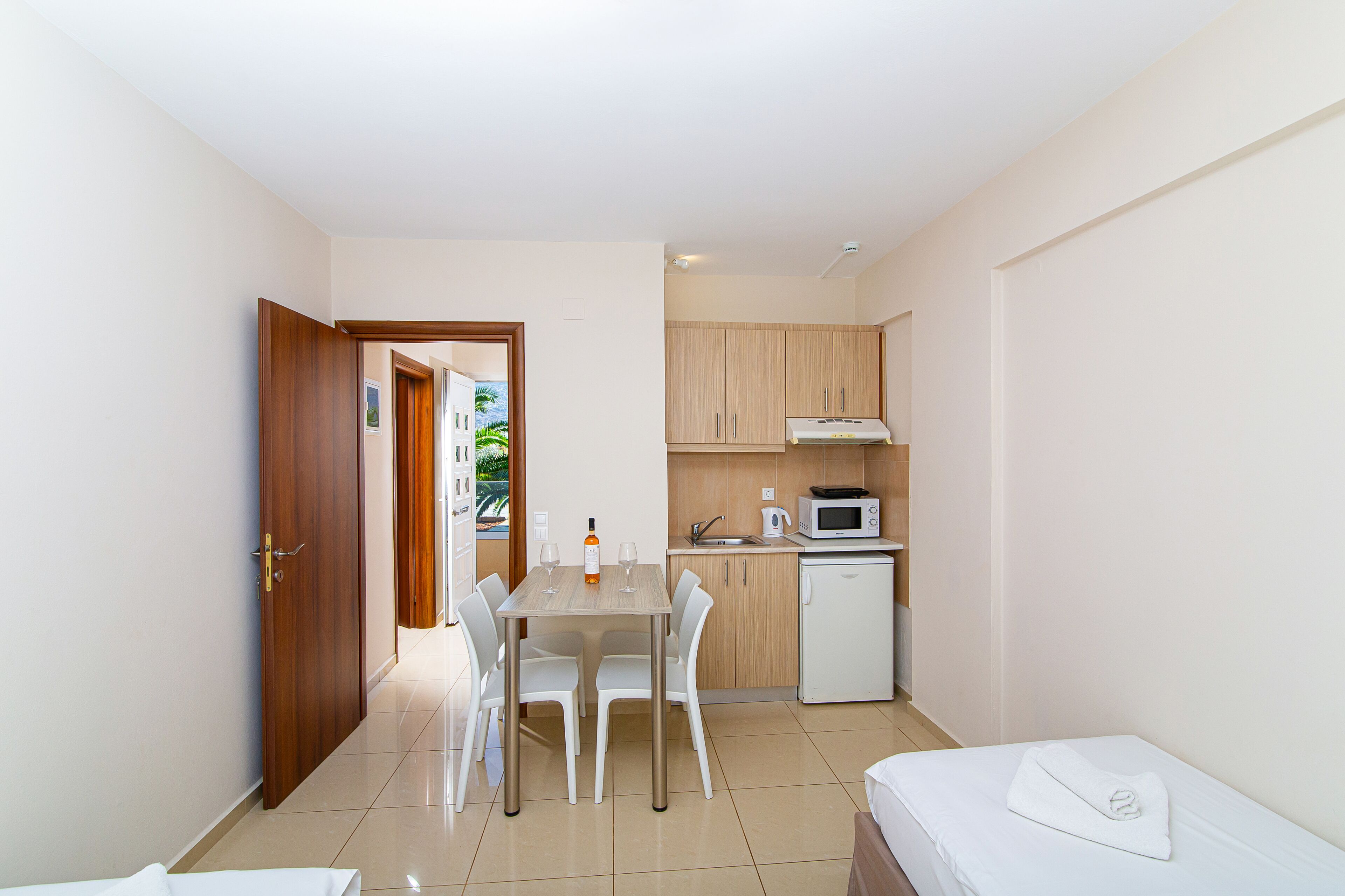 Una habitación compacta con kitchenette, un comedor con mesa y sillas, y una cama con una manta blanca.