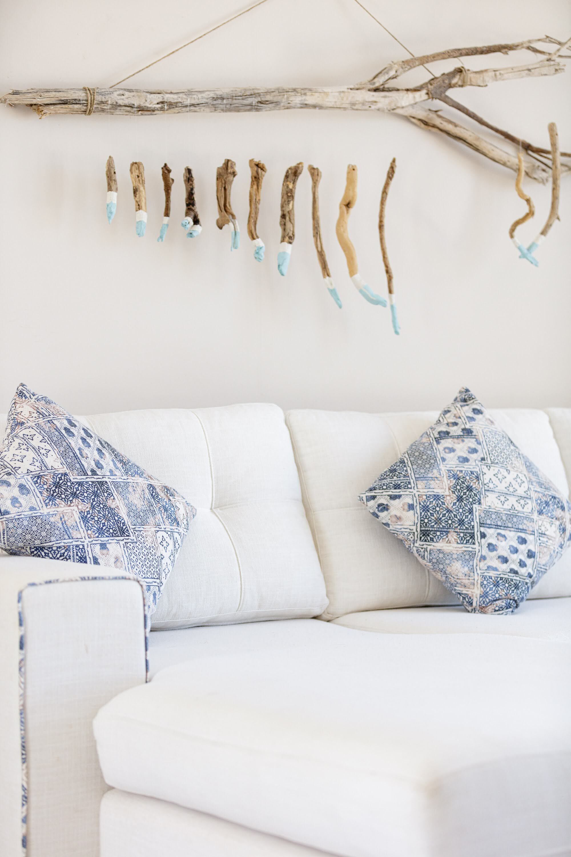 A white sofa with patterned pillows and a branch decoration on the wall.