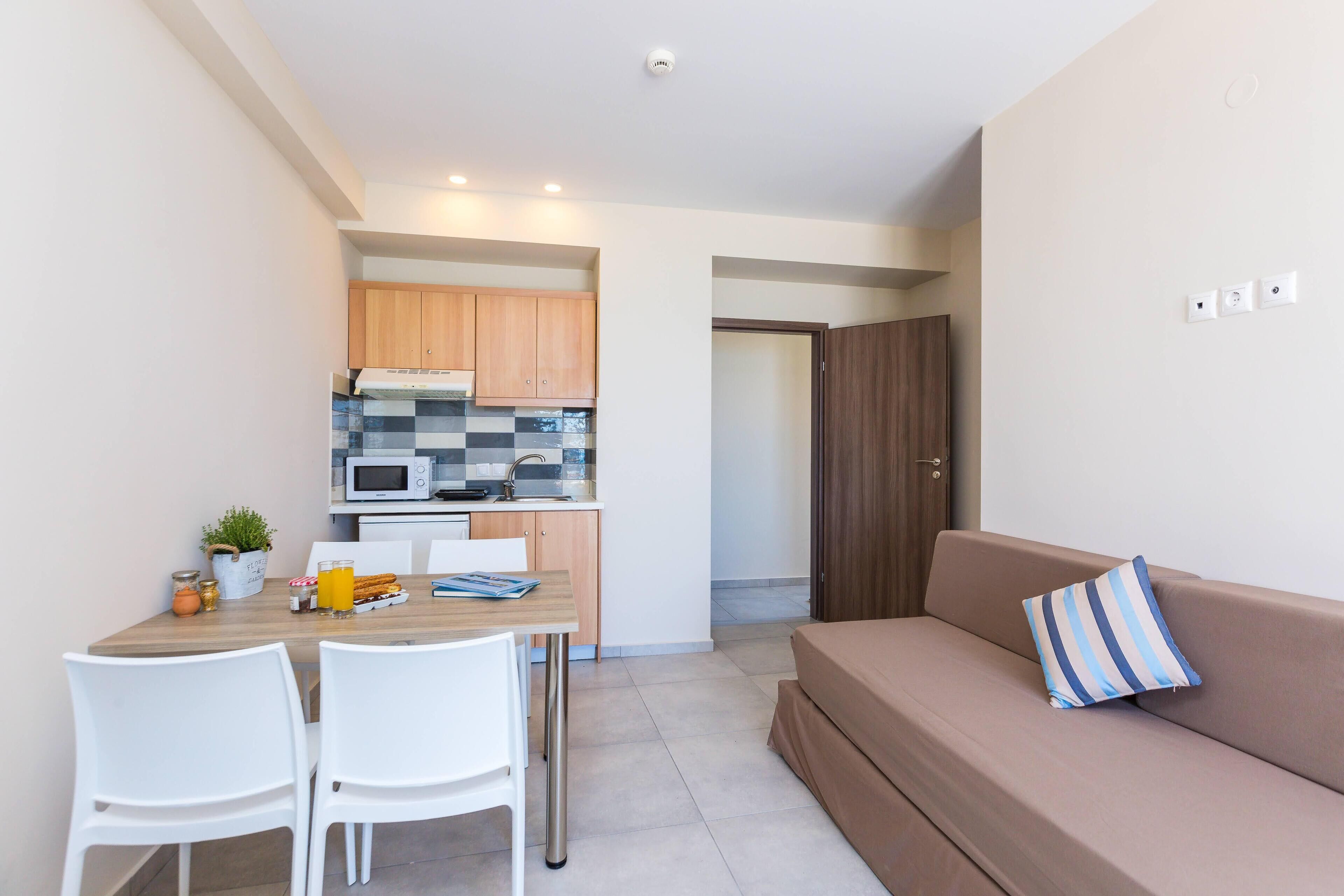Un espacio habitable compacto con kitchenette, una zona de comedor con dos sillas y un sofá con un cojín a rayas.