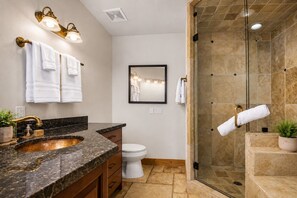 Une salle de bain dotée d’un comptoir en granit, d’un robinet doré, de toilettes blanches, d’une douche en verre et d’un miroir.