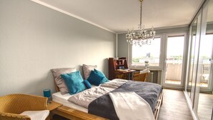 Ein Schlafzimmer mit einem hölzernen Bett, einem Korbstuhl, einem kleinen Tisch und einer Kandelaber.