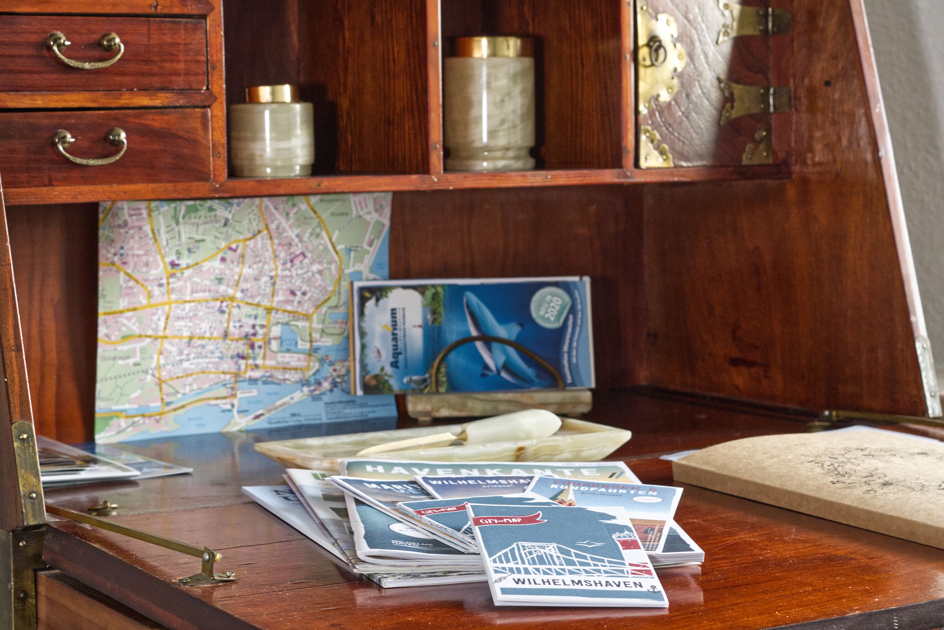 Un bureau en bois, sur lequel on trouve une carte, une boussole et des brochures de voyage.