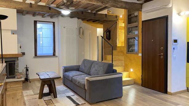 A living room with a grey sofa, wooden floor, stone fireplace, and a staircase leading to a loft. - The Old Fashion House (Cortona)