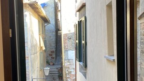 A narrow street with stone buildings, a staircase, and a window with a view of the street. - The Old Fashion House (Cortona)