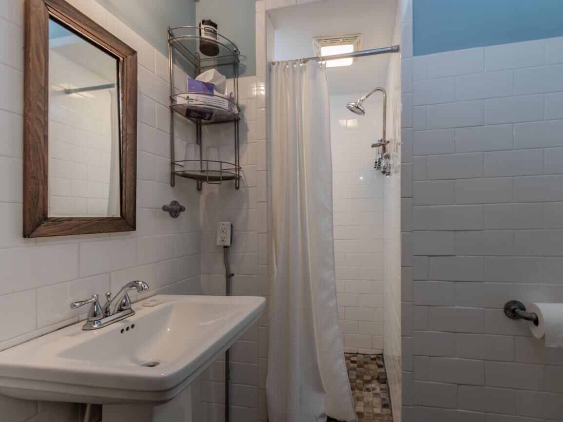 A bathroom with a white sink, a mirror, a shower with a curtain, and a towel rack.