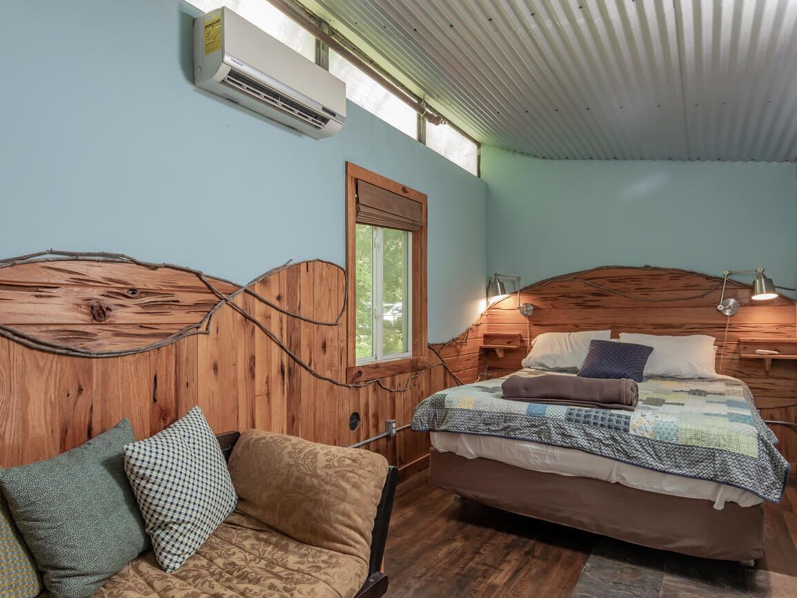 Une chambre confortable avec une tête de lit en bois, un lit recouvert d’une courtepointe, une table de chevet et une fenêtre donnant sur un beau paysage.