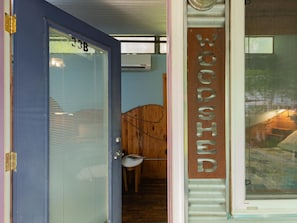 Ein Zimmer mit Holztür mit der Aufschrift 'WOOSED', einem Fenster mit Jalousien und einem kleinen Tisch mit Stuhl.