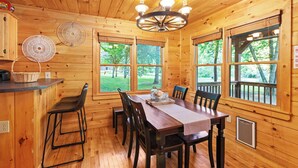 Een houten chalet met een eettafel, stoelen, een kroonluchter en grote ramen met uitzicht op een tuin.