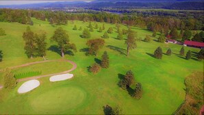 Vista aérea de un campo de golf con búnkeres de arena, árboles y un edificio a lo lejos.