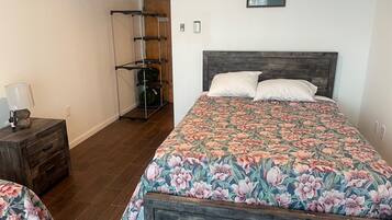 Quarto com colcha florida, cabeceira de madeira e um suporte de metal com malas.