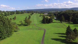 Campo de golf con un sendero despejado, rodeado de árboles y una vista distante de colinas.