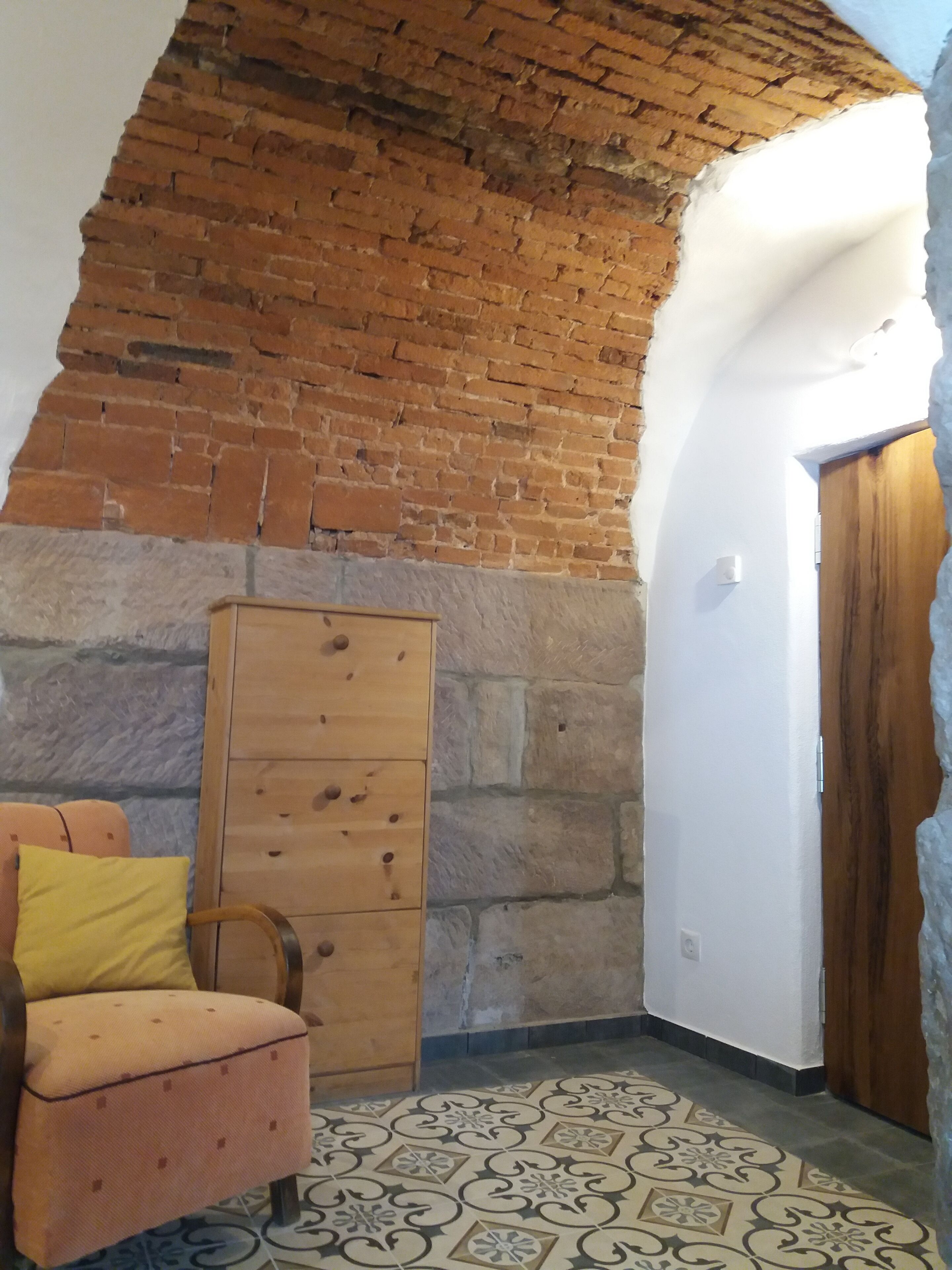 Une pièce avec un mur en briques, une armoire en bois, un sol à motifs et une porte en bois.
