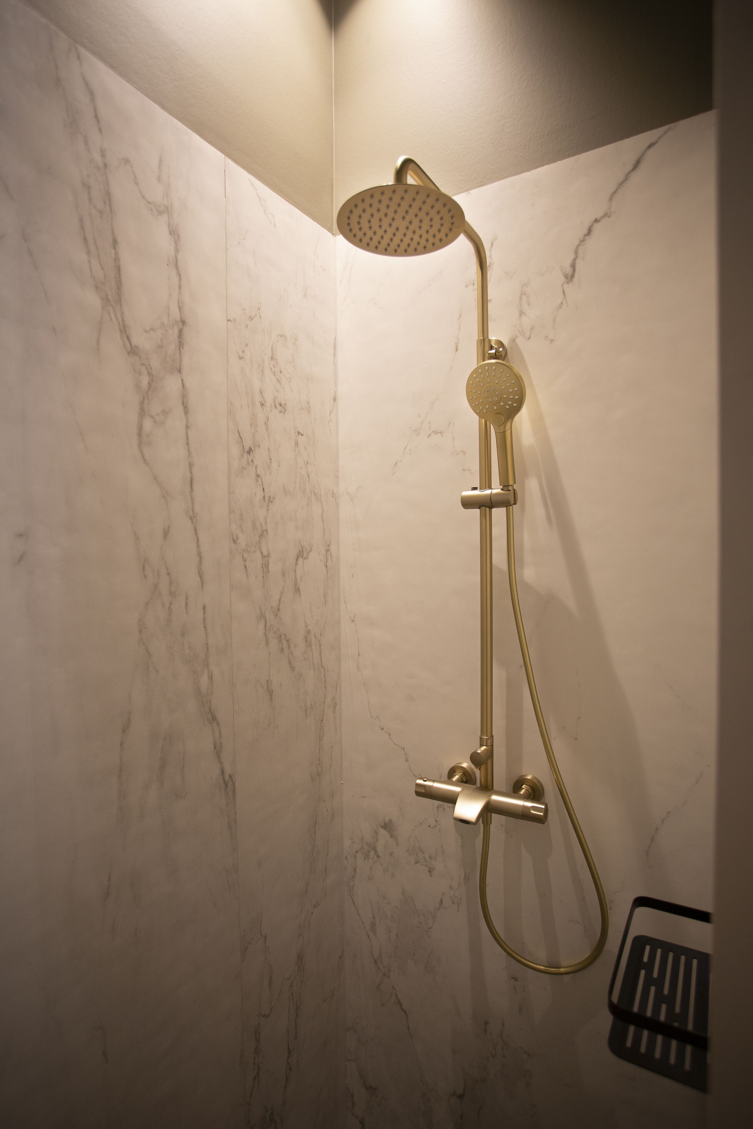 A corner shower with a handheld showerhead and a handheld hose, mounted on a marble wall.