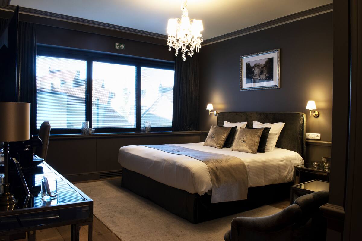 A hotel room with a large bed, a desk, a chair, and a chandelier.