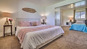 Une chambre avec un grand lit, deux tables de chevet avec des lampes, une décoration murale et une vue sur une autre pièce par une porte ouverte.