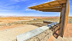 Un paysage désertique avec une structure métallique dotée d’un toit incliné et d’un banc en béton.