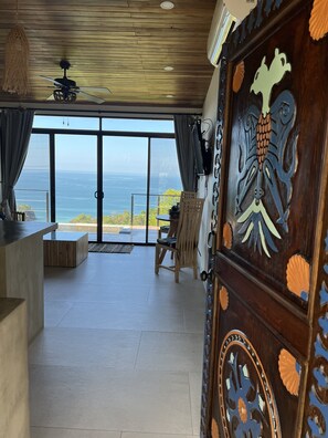 A spacious room with a large sliding glass door leading to a balcony with a view of the ocean.