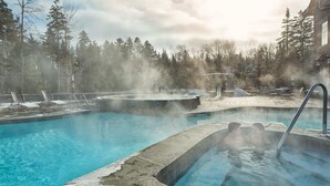 Un espace de piscine d'eau chaude avec un dispositif de diffusion de vapeur, entouré d'arbres et d'un bâtiment.