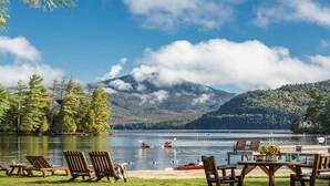 Une vue sur le lac avec des personnes pratiquant le kayak, une jetée avec des chaises et des tables, et une montagne en arrière-plan.
