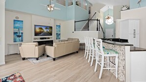 A modern living room with a sofa, TV, and a dining area with chairs. - 6 BR, 5 BA, Close to Disney, Salt Water Pool, Games Room, POOL HEAT INCLUDED ! (Kissimmee)