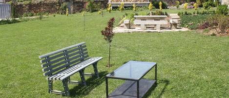 Un espace extérieur verdoyant avec un banc en bois et une table dont le plateau est en verre.
