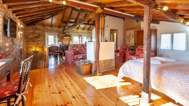Een rustiek houten interieur met een stenen muur, houten balken, een eethoek en een bed met bloemenbedrukking.