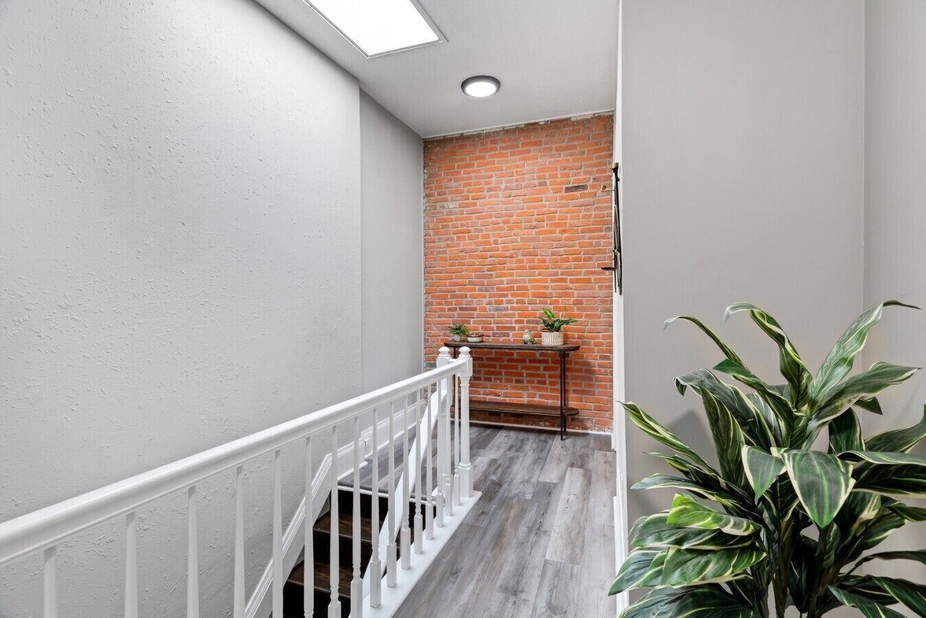 A hallway with a white railing, a brick wall, and a wooden floor.