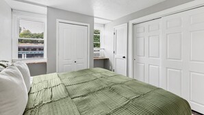 A bedroom with a bed, two white doors, and a window with blinds. - The Loft on Main | Steps to Dining & Nightlife (Saint Charles)