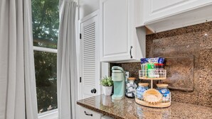 A kitchen with white cabinets, a granite countertop, a Keurig coffee maker, a small potted plant, and a spice rack with jars. - The Loft on Main | Steps to Dining & Nightlife (Saint Charles)