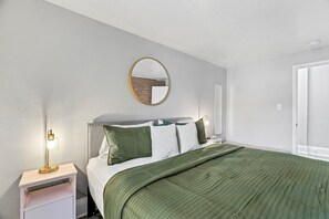 A bedroom with a bed, a bedside table, a lamp, a mirror, and a door. - The Loft on Main | Steps to Dining & Nightlife (Saint Charles)