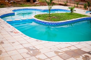 A swimming pool with a tiled edge and a small grassy island in the center. - Self-contained bed sitter overlooking a beautiful scenery in an animal farm. (Lilongwe)
