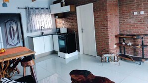 A compact kitchen with white cabinets, a black stove, and a brick wall. - Self-contained bed sitter overlooking a beautiful scenery in an animal farm. (Lilongwe)