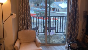 Une pièce dotée d’une grande porte-fenêtre coulissante donnant sur un balcon avec vue sur un espace extérieur enneigé, ainsi que d’un fauteuil beige et d’une lampe.