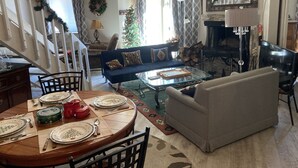 Un salon chaleureux comprenant un coin repas, une cheminée et un escalier menant à un autre niveau.