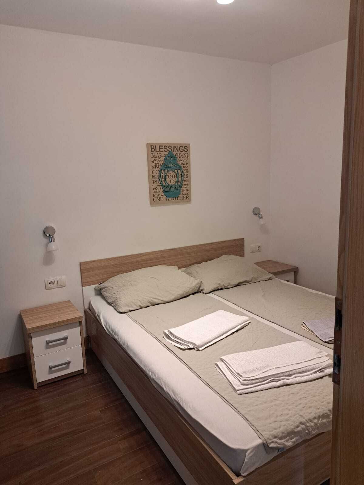 Un dormitorio con cama de madera, dos mesitas de noche, una lámpara de pared y una cita inspiradora enmarcada.