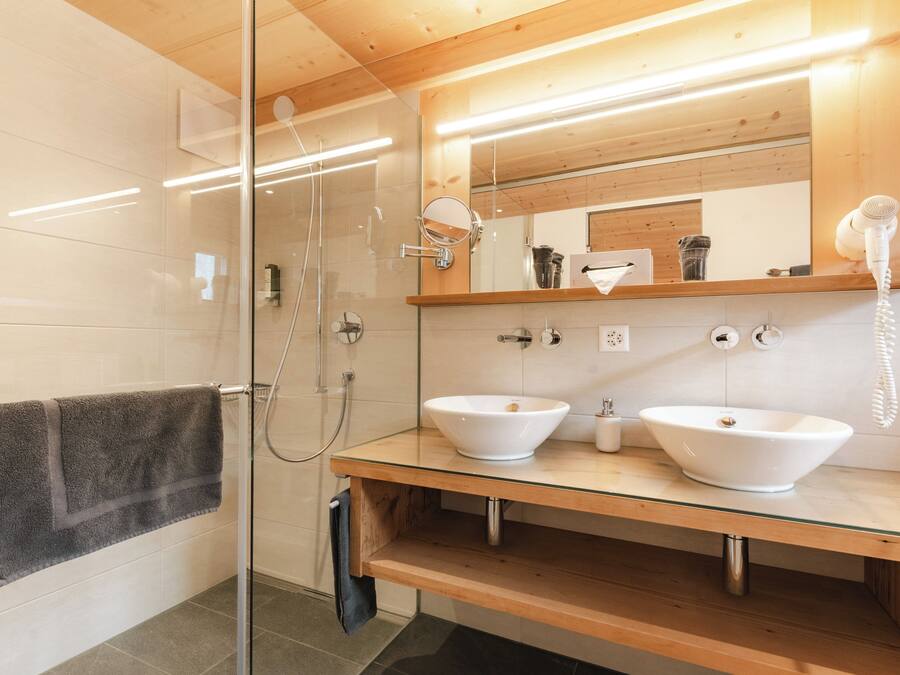 A modern bathroom with two sinks, a glass shower enclosure, and a wooden vanity.