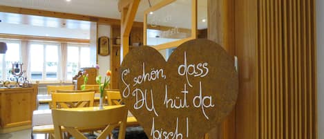 A wooden interior with a heart-shaped sign with text, wooden furniture, and a window with curtains.