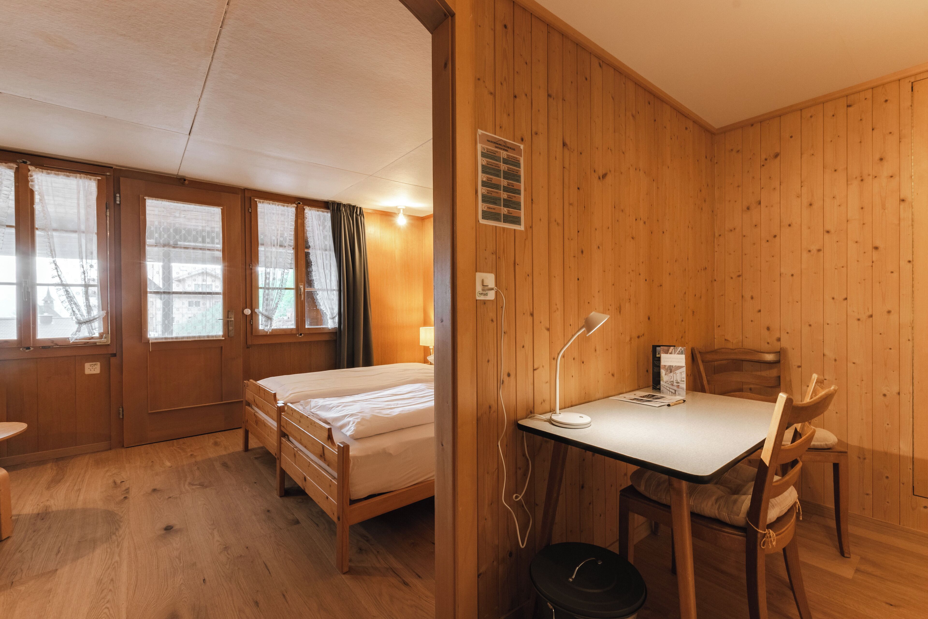 Een kamer met houten lambrisering, twee bedden, een bureau en een stoel.