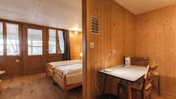 Een kamer met houten lambrisering, twee bedden, een bureau en een stoel.