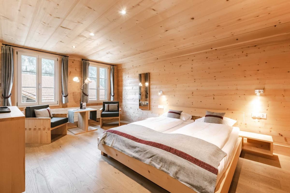 Une chambre à coucher de style cabane en bois, avec un grand lit, un bureau, une chaise et une fenêtre avec des rideaux.