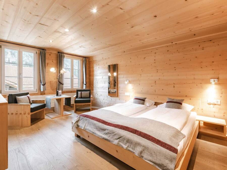 Un dormitorio tipo cabaña de madera con una cama grande, un escritorio, una silla y una ventana con cortinas.