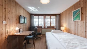 Una habitación con paneles de madera, una cama, un escritorio, una silla, un televisor y ventanas.