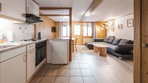 Ett kompakt kök med diskmaskin, spis och ett litet kylskåp. Det finns en matplats med ett bord och stolar, och en soffa i vardagsrummet.